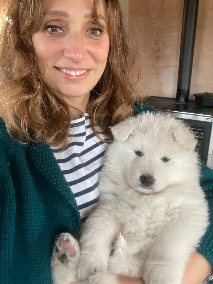L'éleveuse tient dans ses bras un chiot Berger Blanc Suisse devant le poêle de la maison